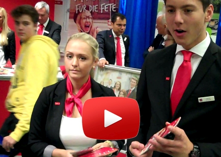 Szene aus dem Video mit Anna Pilarsiki und Justin Schnabl am Infostand der Sparkasse am Niederrhein. Im Hintergrund vor dem „Knete für die Fete“-Plakat Sparkassenchef Giovanni Malaponti.