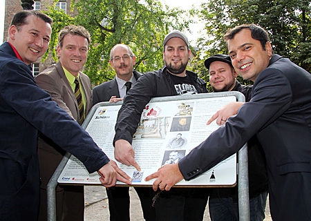 Stadtarchivar Christoph Spilling, Stefan Oppermann (Projektkoordinator der Stadt Moers), Bürgermeister Christoph Fleischhauer, Giovanni Malaponti (Vorstandsvorsitzender Sparkasse am Niederrhein), Markus Grimm und Benedikt Schmitz kleben am Moerser Schloss den erste QR-Code auf die Geschichtsstation. 