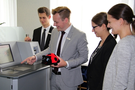 Lars Kruse, Tobias Hansmeier, Kristina Hafemeister und Annika Schmitz zeigen Lucy die Zählmaschine, in die die Kinder am Weltspartag ihre Münzen schütten dürfen.