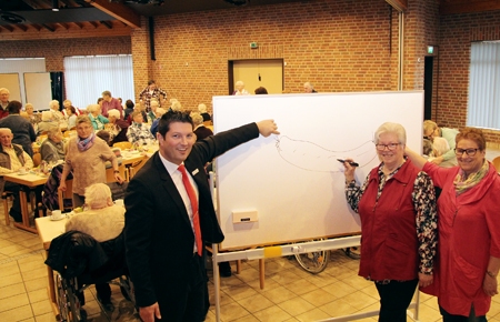 Was Liesel Paßmann (Mitte) auf die neue Tafel gemalt hat, erraten die Besucher des ökumenischen Seniorennachmittags schnell: „Alles hat ein Ende, nur die Wurst hat zwei“. Zur Lösung tragen Oliver Heger von der Sparkasse am Niederrhein (links) und Renate Hegmann (rechts) bei, denn sie zeigen auf die zwei Enden der Wurst.