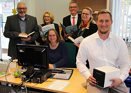 Marco Schinköther, IT-Spezialist der Gemeinde Alpen, (rechts vorne) installierte die neue Speicherbox der Bücherei. Anlässlich der Inbetriebnahme luden (v.l.n.r.) André Emmerichs und Kerstin Pieper Sparkassenvorstand Bernd Zibell und Geschäftsstellenleiterin Kathrin Hüsch zum Besuch ein. Am PC: Mechthild Heining, eine von 25 Ehrenamtlichen des Bücherei-Teams. 