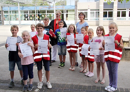 Stolz zeigen die zu Junior-Rettern ausgebildeten Schülerinnen und Schüler der Viktor-Gemeinschaftsgrundschule ihre Urkunden. Links vorne: Tom, Chayenne und Friethjof. Beim Besuch von Cornelia Gietmann (hinten, links) von der Sparkasse am Niederrhein demonstrierten sie ihr Know-how in Sachen Erste Hilfe. Schulleiterin Martina Salewski (r.) bedankte 