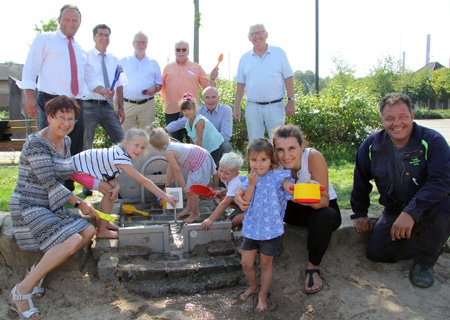 Eröffnung der Matschanlage auf dem Ossenberger Dorfplatz (hinten, v.l.n.r.): Frank-Rainer Laake (Sparkasse) Bürgermeister Frank Tatzel, Helmut Hofmann, Hans Dröttboom (beide Heimatverein Herrlichkeit Ossenberg), Norbert Mülders (Solvay) und Bernward Wißenberg (ebenfalls Heimatverein Herrlichkeit Ossenberg). Vorne links: Dr. Gisela Irawan (Heimatverein und ganz rechts: Metallbauer Oliver Rettig, links daneben Feray Ökce sowie Kinder des Kindergartens St. Mariä Himmelfahrt.