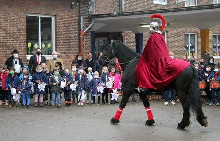 Sankt Martin trabt auf seinem Rappen über den Schulhof der Grundschule St. Peter. Die vom Martinskomitee entwickelte coronakonforme Variante der Martinsfeier machte die Kinder glücklich. Vereinspräsident Clemens Geßmann (hinten links) bedankte sich bei Sparkassenvorstand Frank-Rainer Laake (daneben) für die finanzielle Unterstützung. Ehrenpräsident Heinz-Dieter Bartels genoss das Ritual, und Schulleiterin Michaela Joost lobte ihre Schüler: „Ihr seid für mich alle kleine Sankt Martins.“