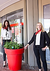 Kerstin Merker (links) und Katrin Steffans, die Leiterinnen der Geschäftsstelle an der Poststraße, freuen sich über den leuchtend roten Pflanzkübel vor der Türe. 