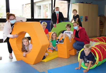 Die aus Schaumstoff-Bausteinen zusammenfügbare Hindernisbahn ist die neue Attraktion in der Turnhalle der Kita Wirbelwind. Das demonstrierten Leiterin Kathrin Dudek (r.), Jennifer Johlitz (l.) und sechs Vorschulkinder ihrem Gast Roman Schönwald von der Sparkasse am Niederrhein. Die hatte mit einer 1.000-Euro-Spende den Kauf ermöglicht.