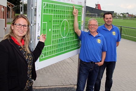 Kathrin Hüsch zeigt auf den Torraum des neuen Kunstrasenplatzes vom FC Viktoria Alpen, Geschäftsführer Jürgen Rischer (Mitte) deutet auf eine Bande. Beide Parzellen erwarb die Sparkasse am Niederrhein auf einer Internet-Plattform und  unterstützte so den Verein mit 1.400 Euro. Pressewart Björn Niedrig betreute den virtuellen Spendenmarathon.