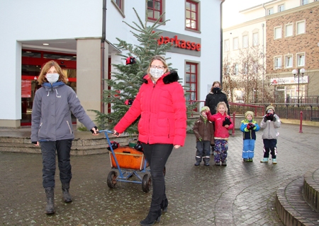 Monika Schmengler (l.) und Kathrin Hüsch ziehen den Bollerwagen mit dem ehemaligen Weihnachtsbaum der Sparkasse. Über den Umzug der Tanne in ihr Wäldchen freuen sich Benno, Carlotta, Max und Lenn sowie Kita-Helferin Sarah Pohland.