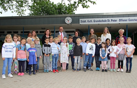 Kleine und große Leute können auf den zwei Schulhöfen der St.-Peter-Grundschule jetzt immer die funkgenaue Zeit ablesen. Die zwei neuen Uhren spendete die Sparkasse am Niederrhein. Das Bild zeigt die Mädchen und Jungen der Klasse 1a mit ihrer Lehrerin Mandy Hübner, Rektorin Michaela Joost, Sparkassenvorstand Frank-Rainer Laake, Jennifer Rott und Britta Jacob vom Förderverein, Erzieherin Laura Wienen sowie Monika van Briel, die Teamleiterin der Offenen Ganztagsschule (v.l.n.r.).