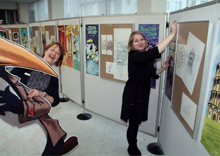 Kathrin Leneke vom Schlosstheater Moers (rechts) und Carmen Müller von der Sparkasse hatten viel Spaß beim Aufhängen der rund 70 Plakate und Skizzen in der Kundenhalle der Sparkasse am Ostring.