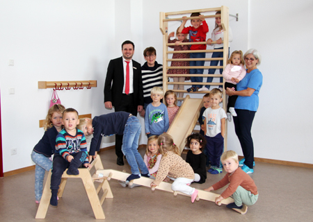 Dawid Sojka von der Sparkasse, Kita-Leiterin Annette Becker und Übungsleiterin Andrea Hagel inmitten einer Kinderschar, die sich über die neuen Geräte in der Turnhalle des Dreikönigskindergartens freuen.