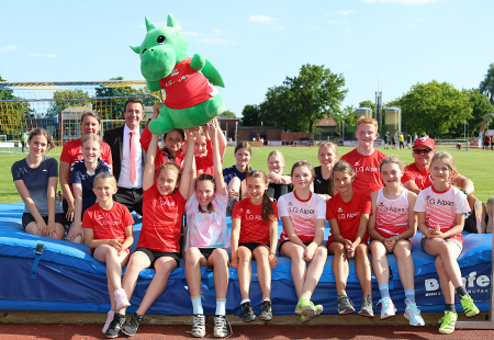 Die Mädchen und Jungen der Leichtathletikgruppe haben das Maskottchen Flippi ins Herz geschlossen. Petra Bohländer (hinten links) und Viktor Walter (rechts mit Kappe und Sonnenbrille) trainieren den U-10 bis U18-Nachwuchs der LG Alpen. Beide hatten Tim Rütters von der Sparkasse zur offiziellen Übergabe des Plüschdrachen eingeladen.