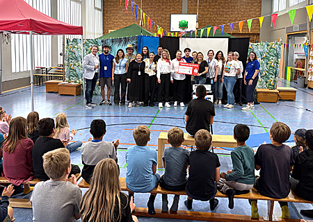 Melanie Peschik und Nadine Lenzkes überreichen Spielpunktleiterin Claudia Deselaers einen symbolischen Scheck. Die Sparkasse am Niederrhein unterstützt die Tummelferien mit 1.000 Euro. Das finden Bürgermeister Christoph Fleischhauer (l.) und die 80 Kids in der Asberger Turnhalle richtig gut.